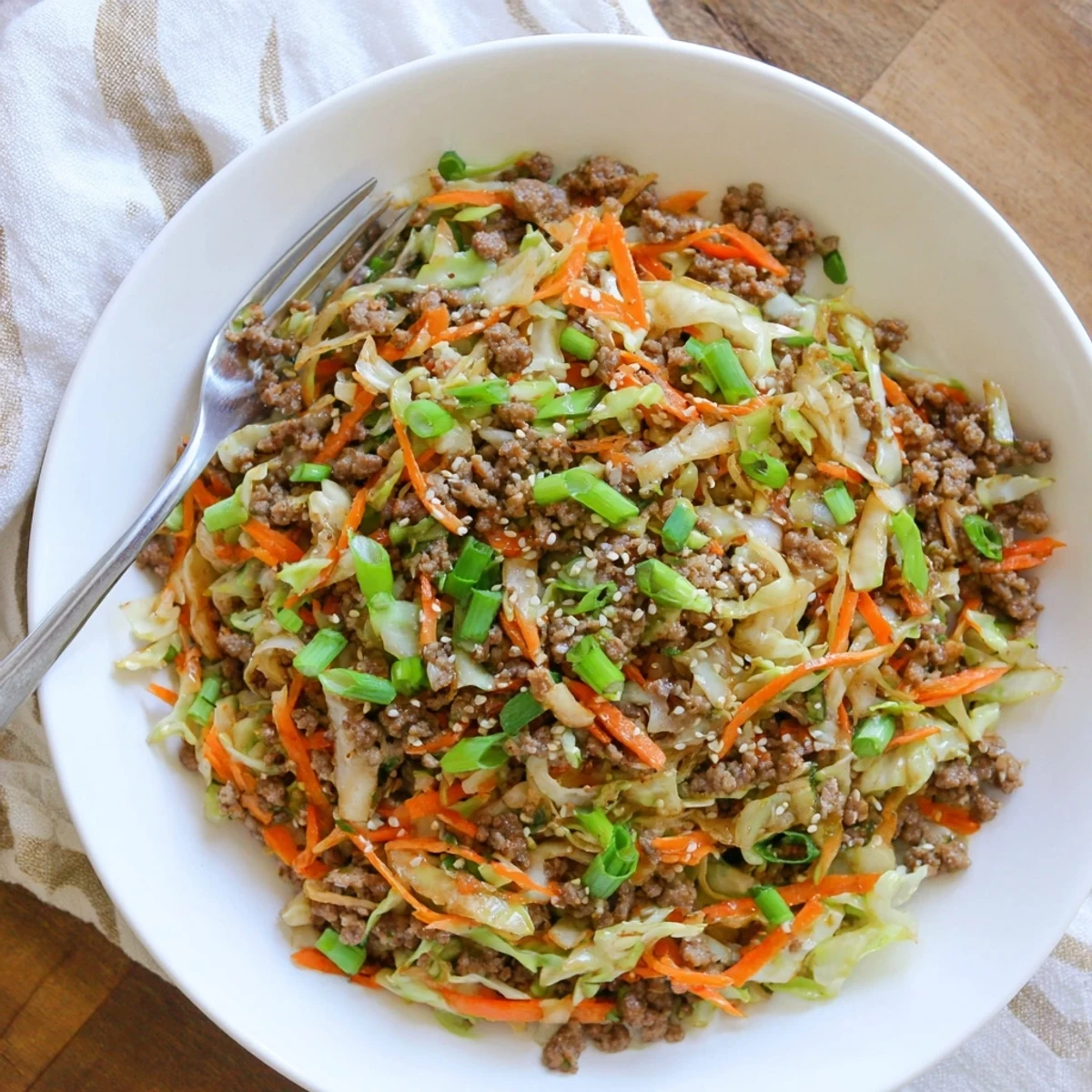 Savory egg roll in a bowl with browned ground pork, shredded cabbage, and carrots in a large white serving bowl