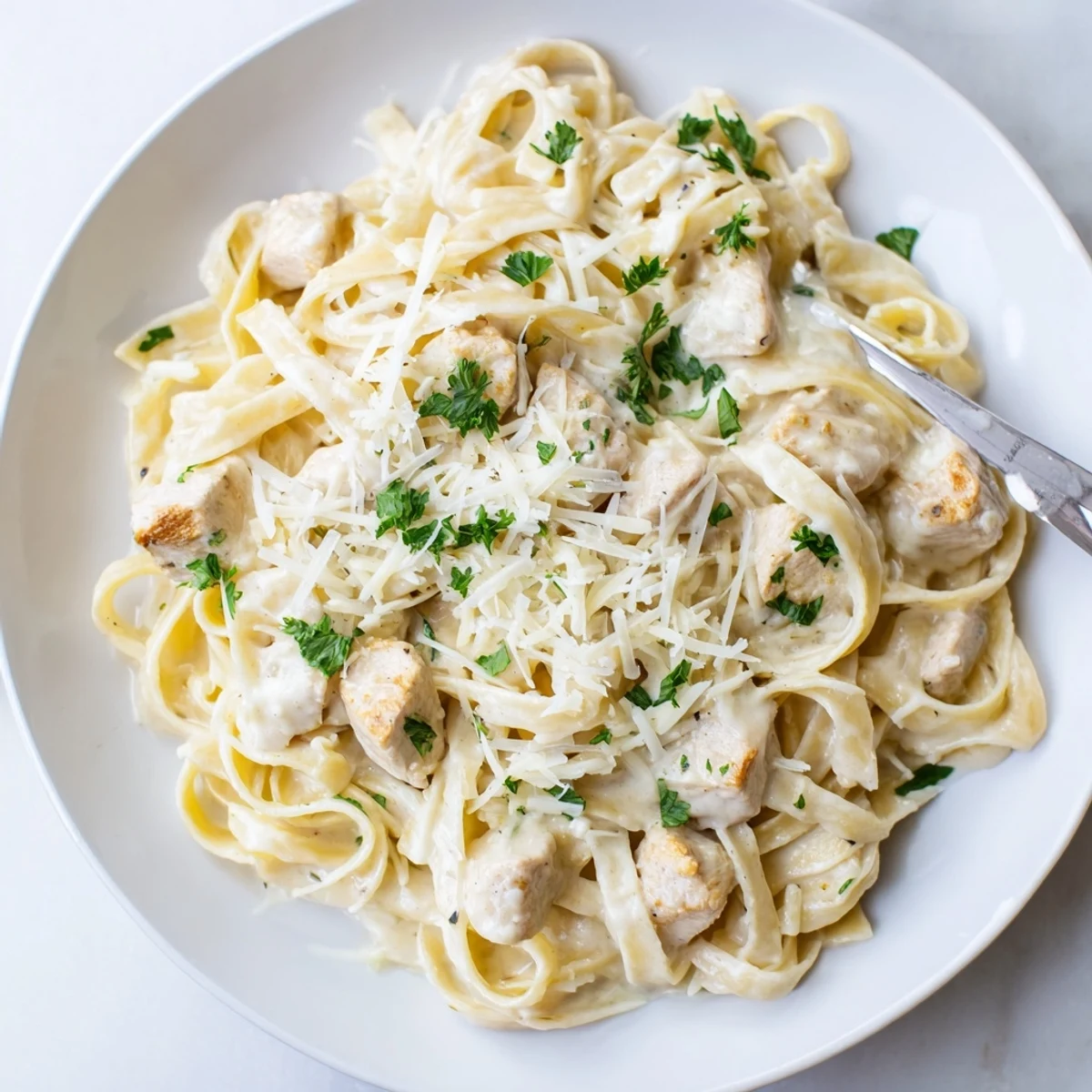 Creamy white garlic Parmesan sauce clings to pasta while savory chicken cubes await.