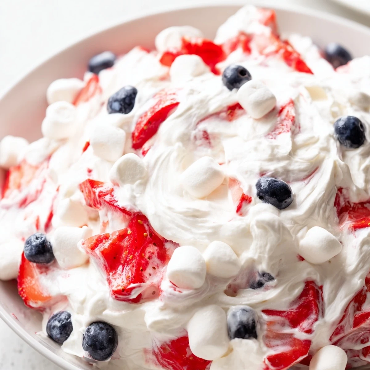 Creamy Red White Blue Cheesecake Salad loaded with fresh strawberries and blueberries in a fluffy bowl
