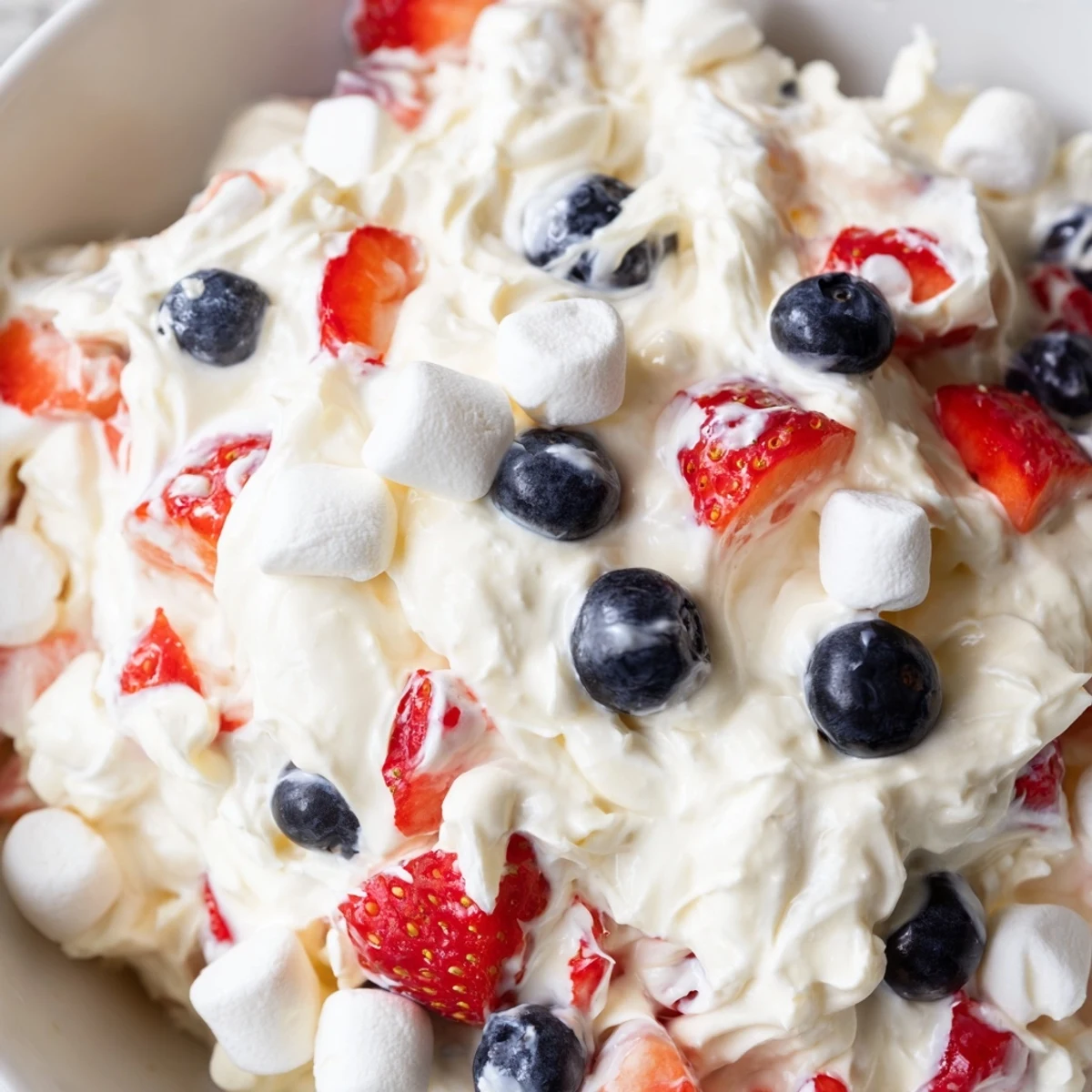 Vibrant Red White Blue Cheesecake Salad scooped into a dessert glass with plump strawberries and whipped cream