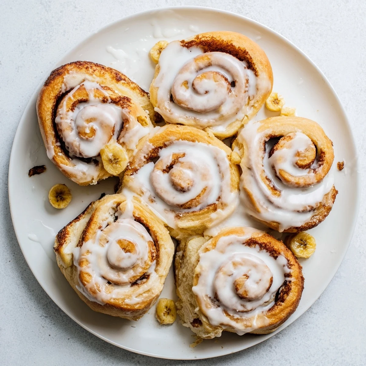 Warm pillowy banana cinnamon rolls with cinnamon swirl and luscious white glaze pooling around them