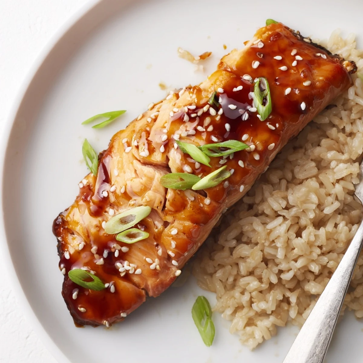 A glossy Baked Teriyaki Salmon plated with sesame seeds and scallions