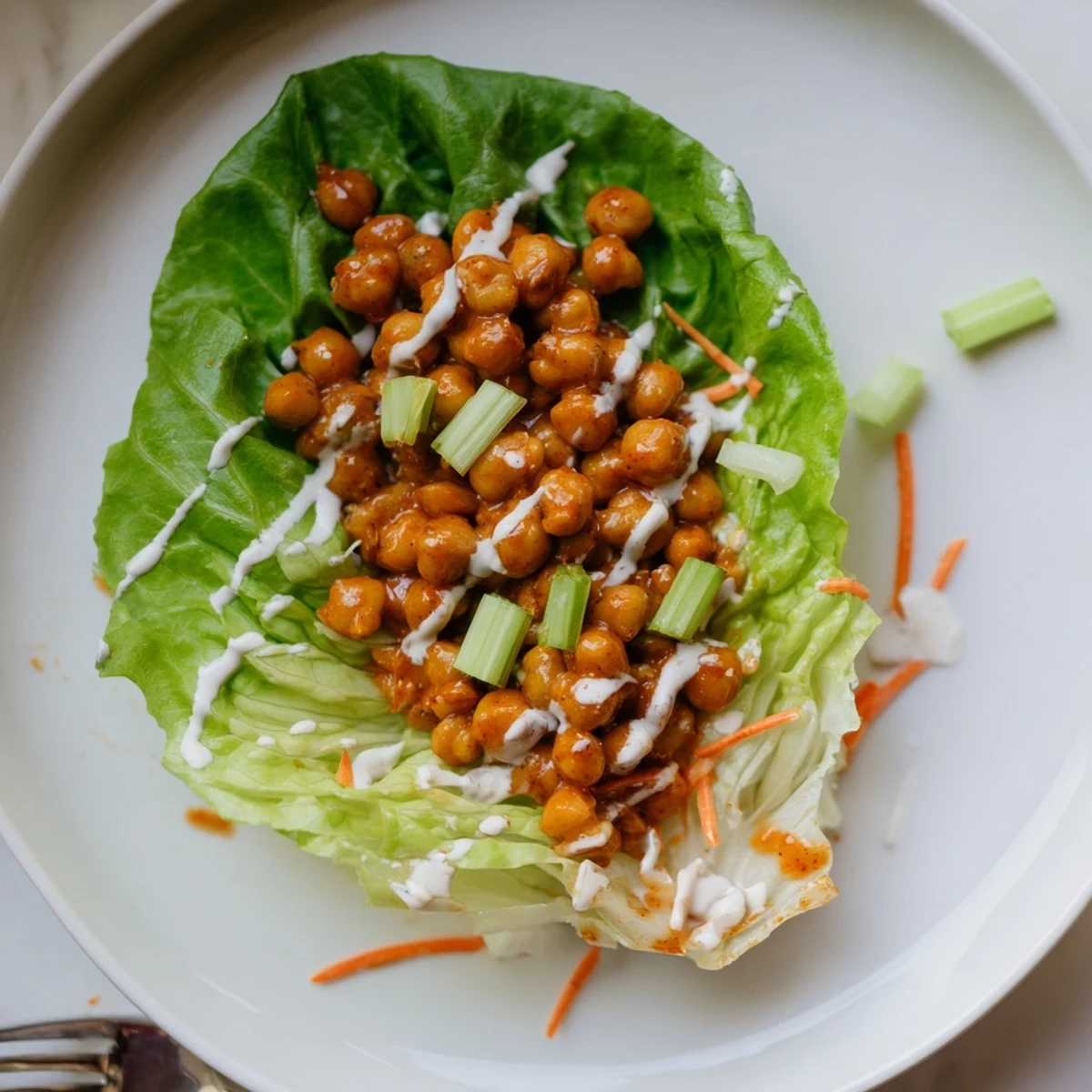 Crisp Buffalo Chickpea Lettuce Wraps garnished with shredded carrots and sliced celery  