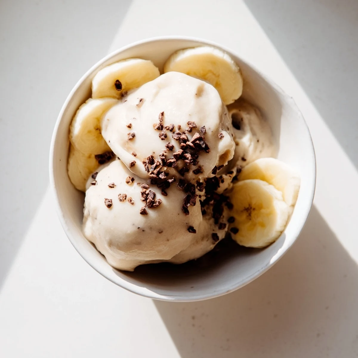 Creamy healthy nice cream scooped into bowls topped with fresh fruit slices and crunchy nuts