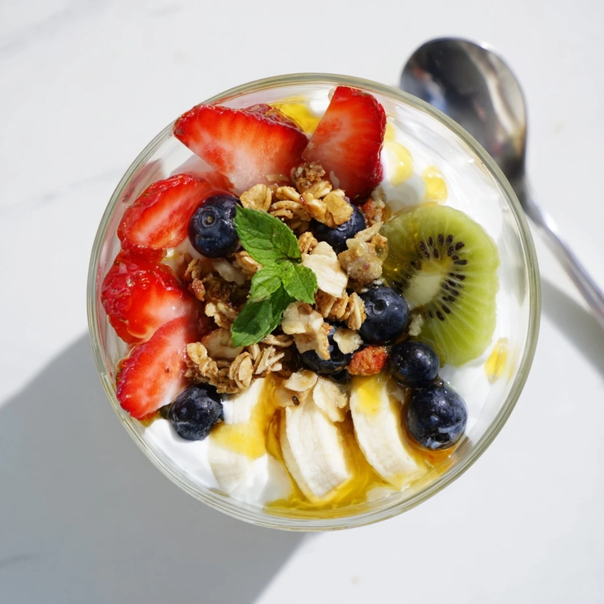 Creamy yogurt parfait recipe topped with granola, fresh fruit, and sweet honey garnish