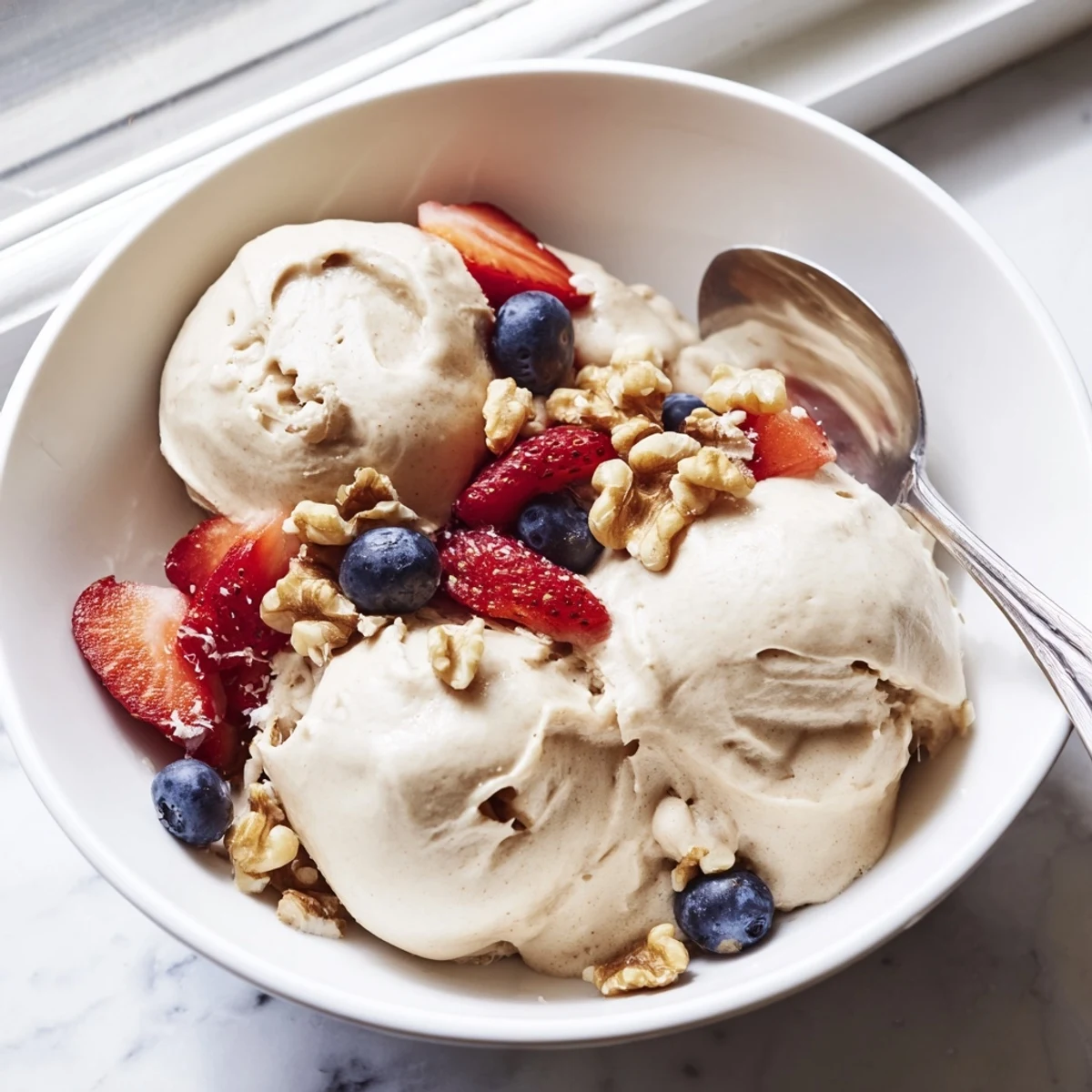 Creamy banana nice cream served in a bowl topped with fresh berries and chopped nuts