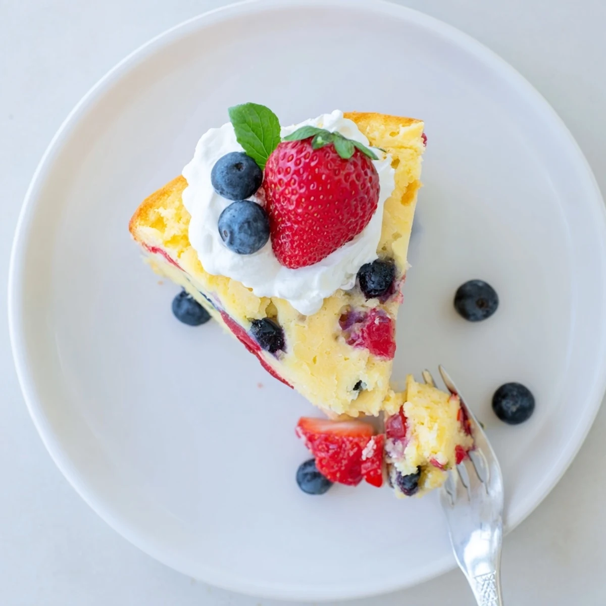 Slice of moist basil berry cake revealing purple berry swirls and green flecks throughout