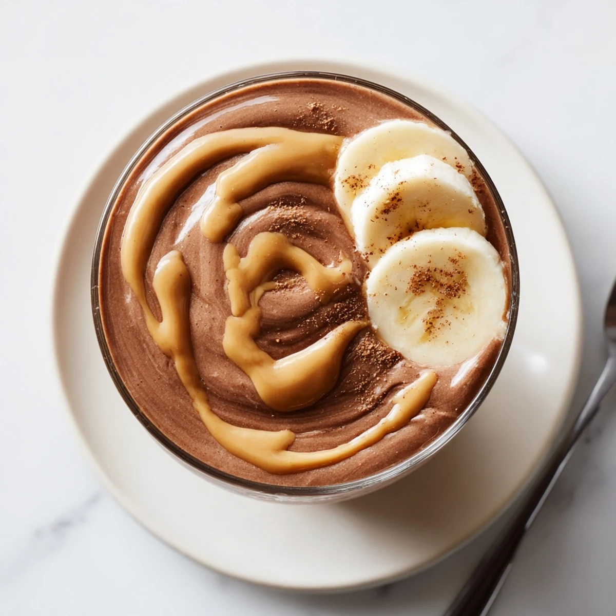 Creamy Chocolate Peanut Butter Banana smoothie in tall glass, topped with sliced banana