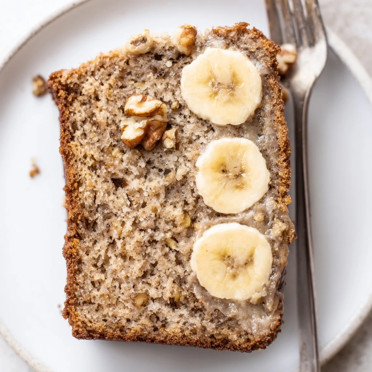 Fork beside moist banana cake topped with cream cheese frosting