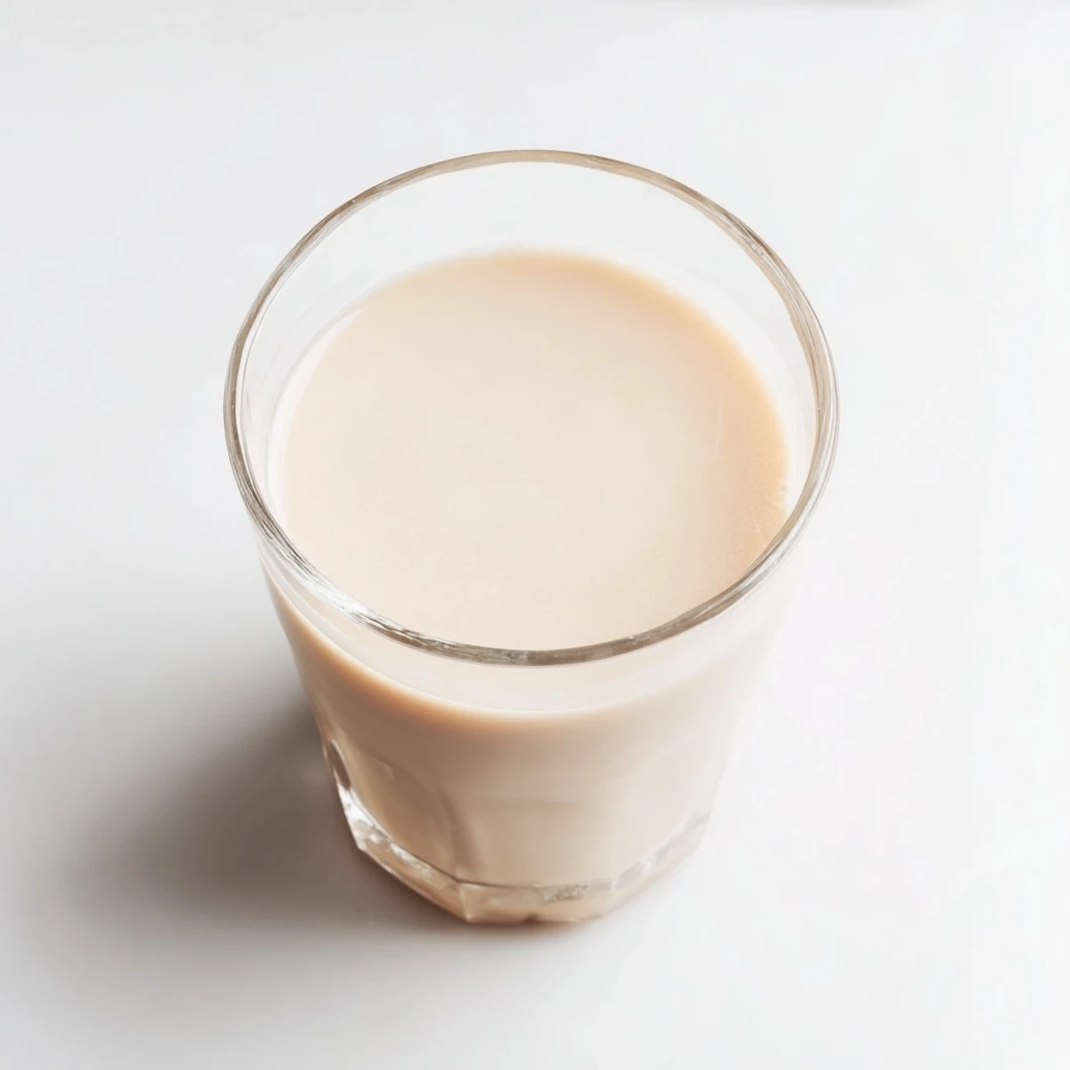 Fresh homemade almond milk poured into a clear glass against a light background