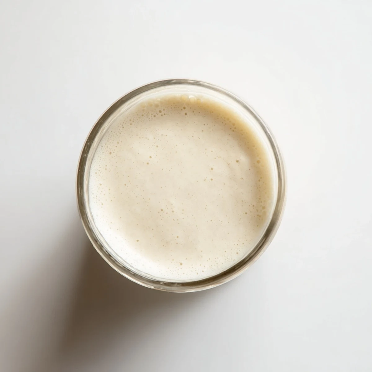 Creamy white almond milk being strained through a nut milk bag into a glass container