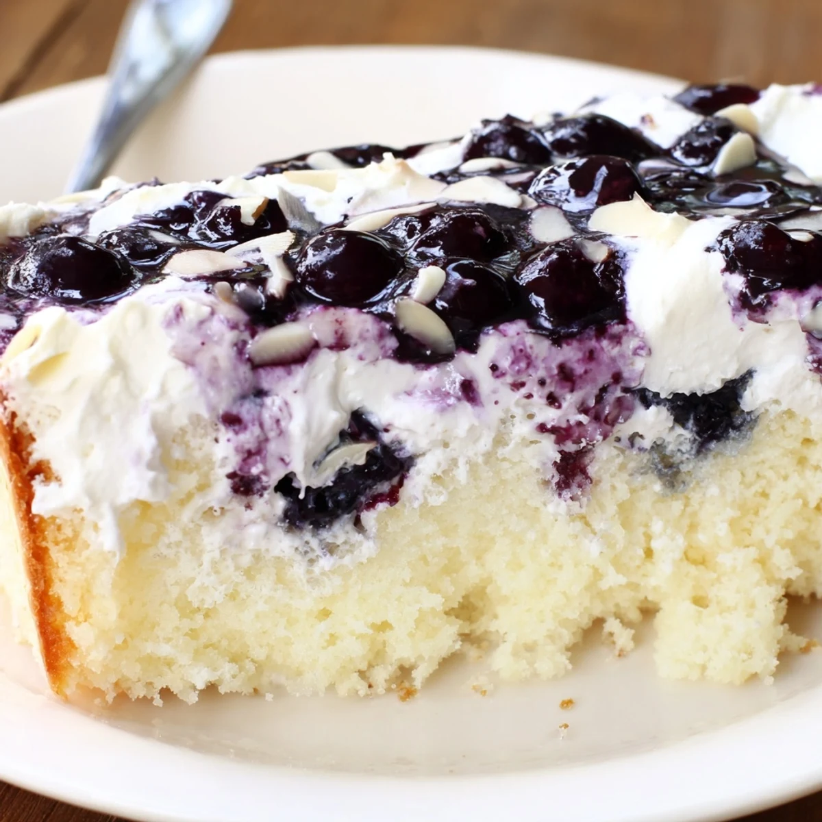 Close-up of Lemon Blueberry Poke Cake With Almond Topping revealing glossy blueberry pockets