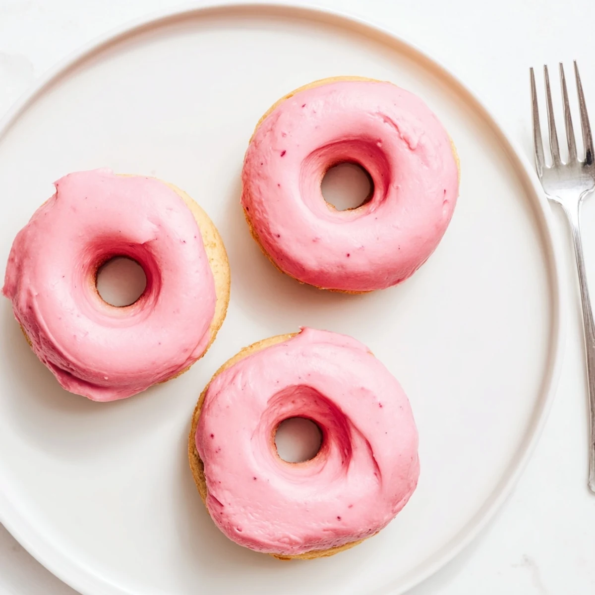 Golden baked strawberry buttercream frosted donuts arranged on a rustic white plate
