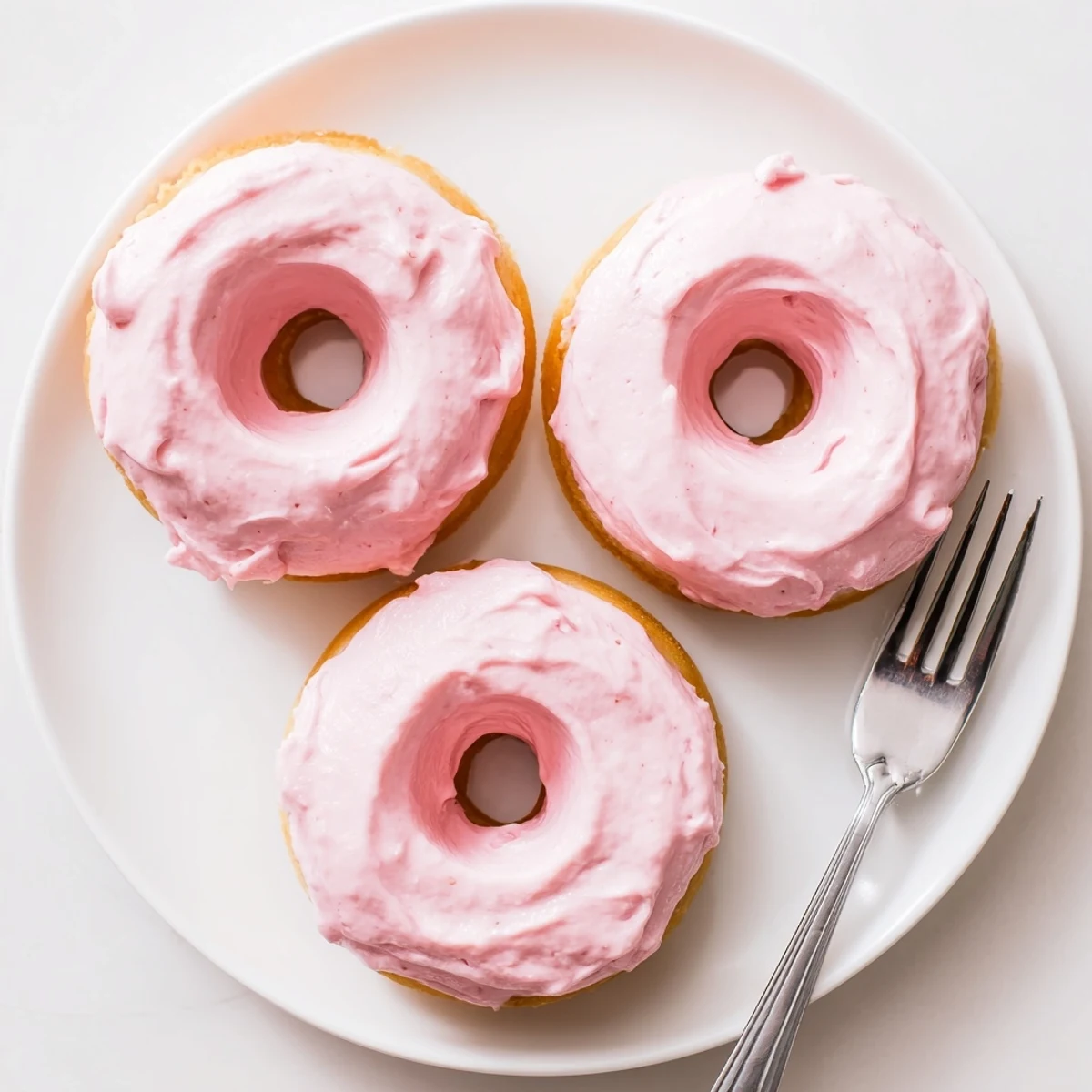 Fresh strawberry buttercream frosted donuts topped with glossy pastel frosting on a cooling rack