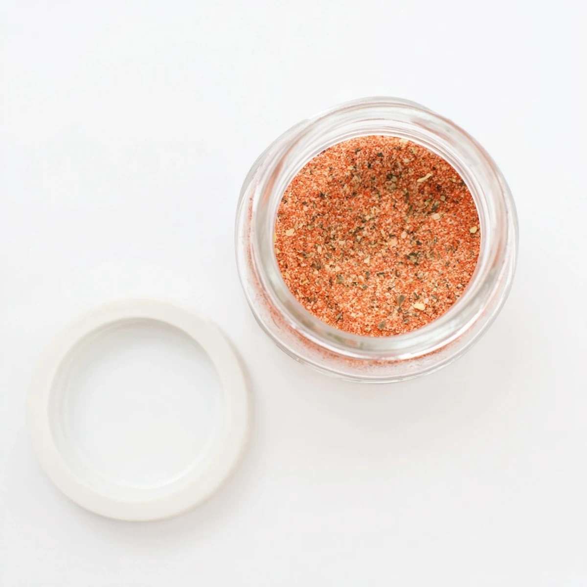 A rustic wooden bowl filled with vibrant red French fry seasoning blend dusted with smoked paprika and dried parsley