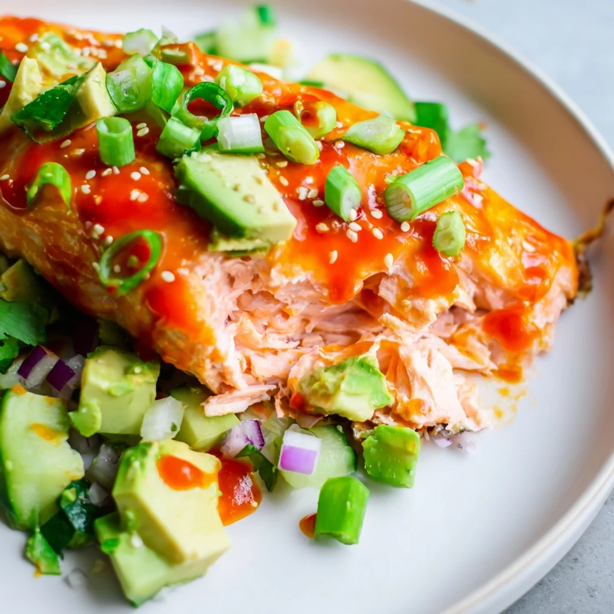 Flaky Bang Bang Salmon resting on a bed of cool avocado cucumber salsa with sesame garnish