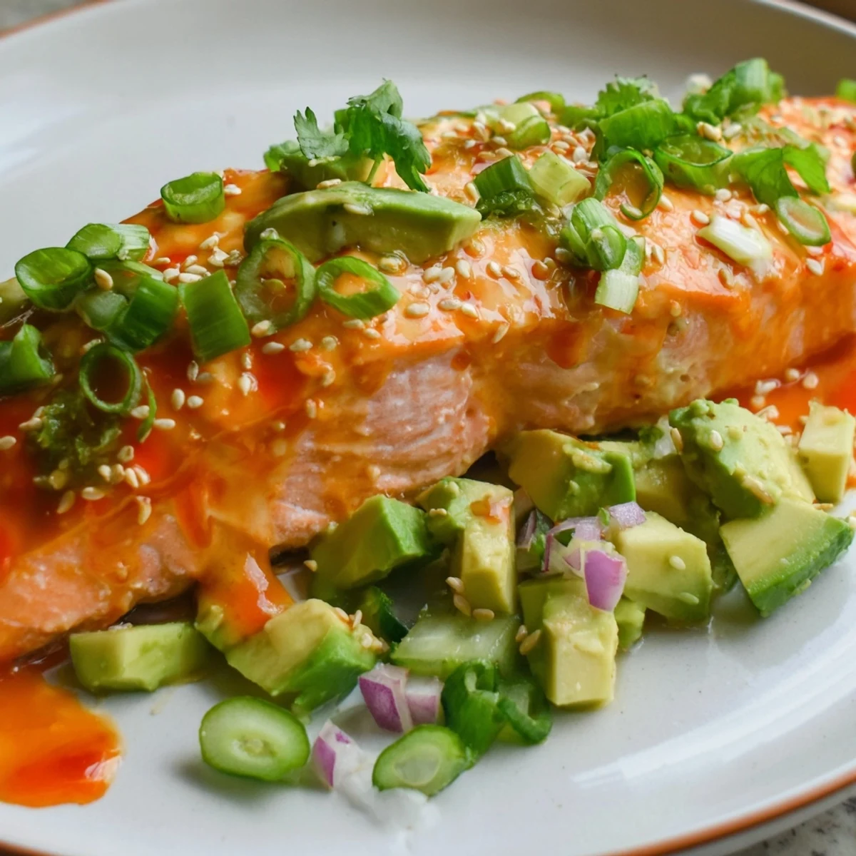 Golden baked Bang Bang Salmon topped with creamy sriracha glaze beside vibrant green avocado cucumber salsa