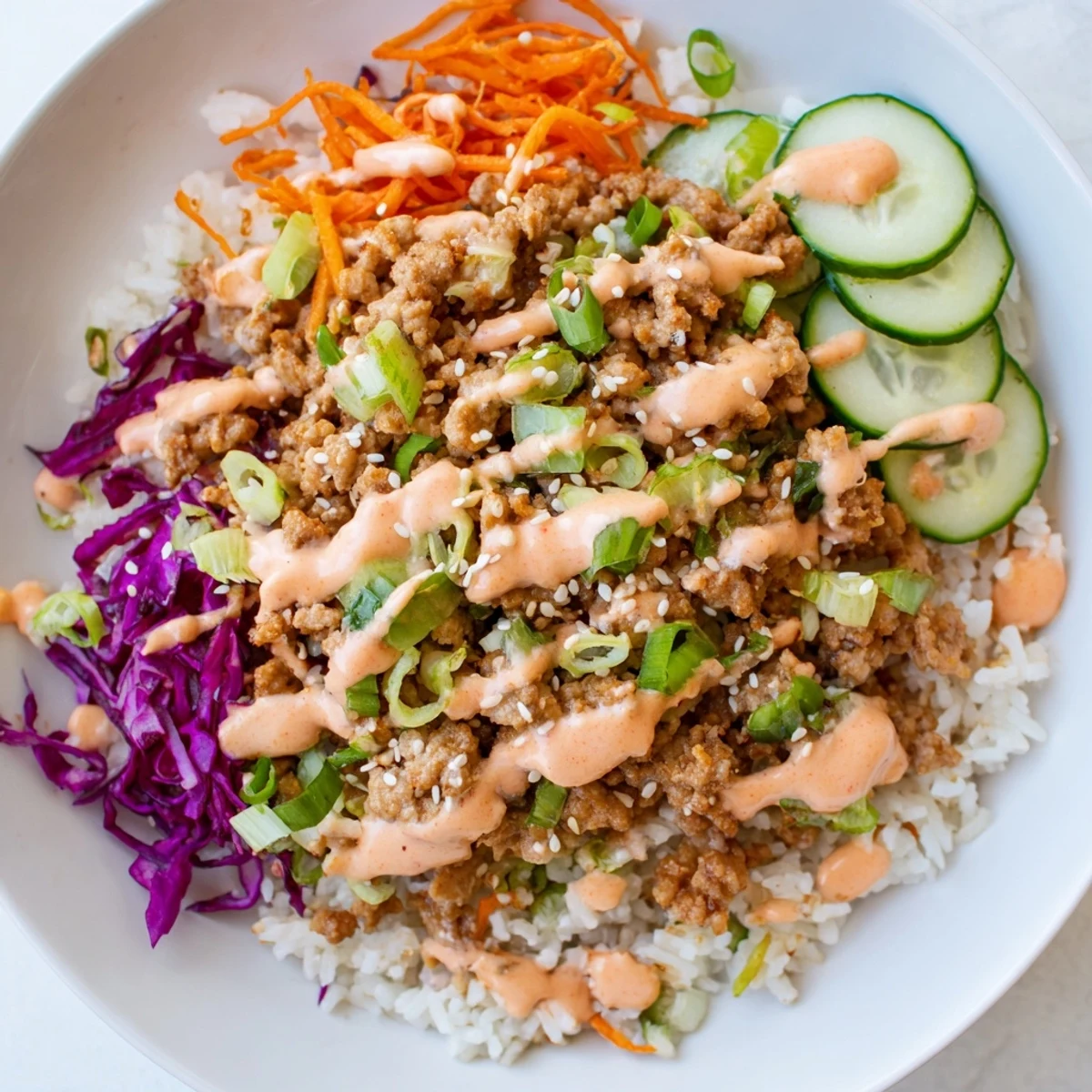 Hearty Ground Turkey Rice Bowls topped with crisp carrots, cucumber, and sweet-spicy sauce