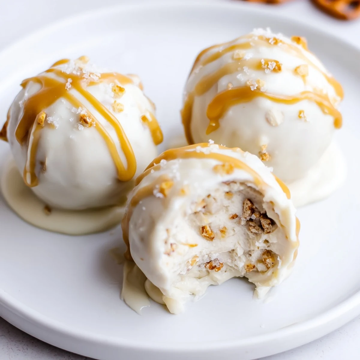 Bite-sized salted caramel pretzel cheesecake balls coated in white chocolate with sticky caramel drizzle