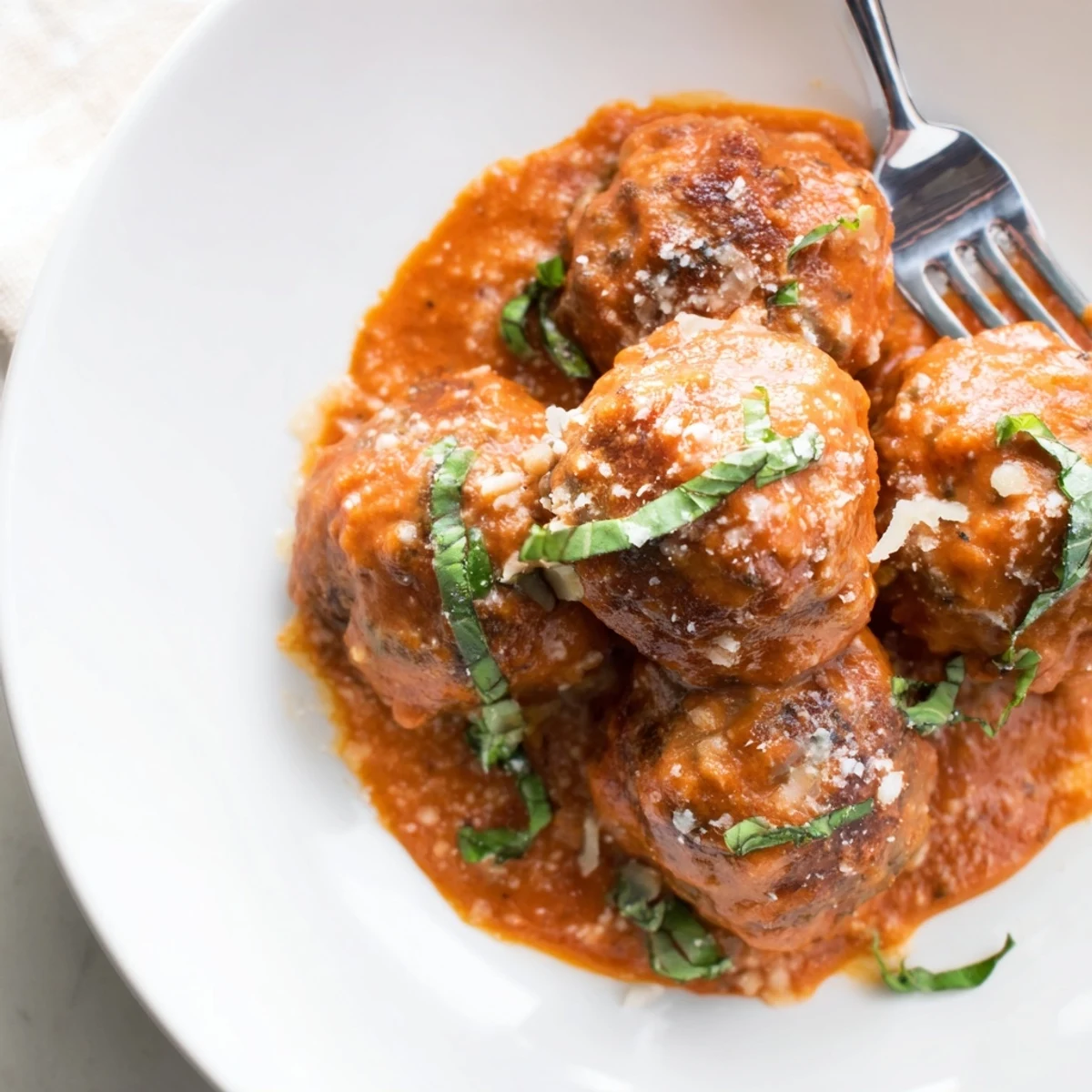 Steaming skillet of creamy tomato basil meatballs garnished with bright green basil leaves