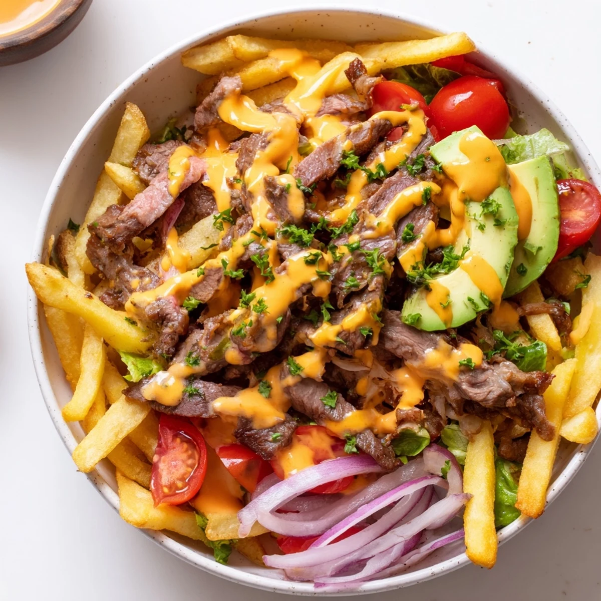 Hearty steak strips and crispy fries bowl topped with fresh sliced avocado