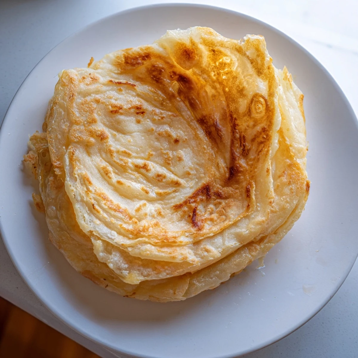 Golden flaky Roti Canai served with curry for a buttery, crispy flatbread experience.  